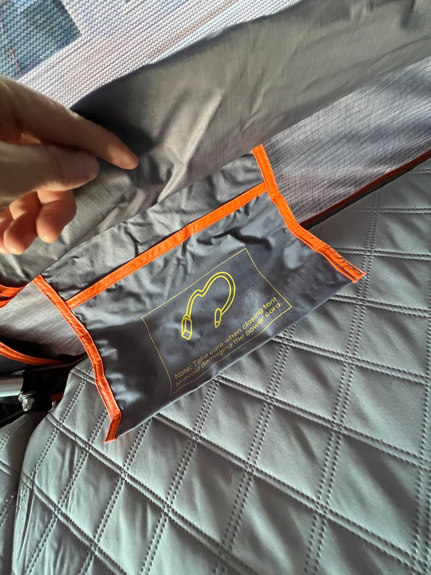 RV rental interior: a safety note on a pouch warns to protect the power cord when closing the tent, by quilted bedding. — photo 11
