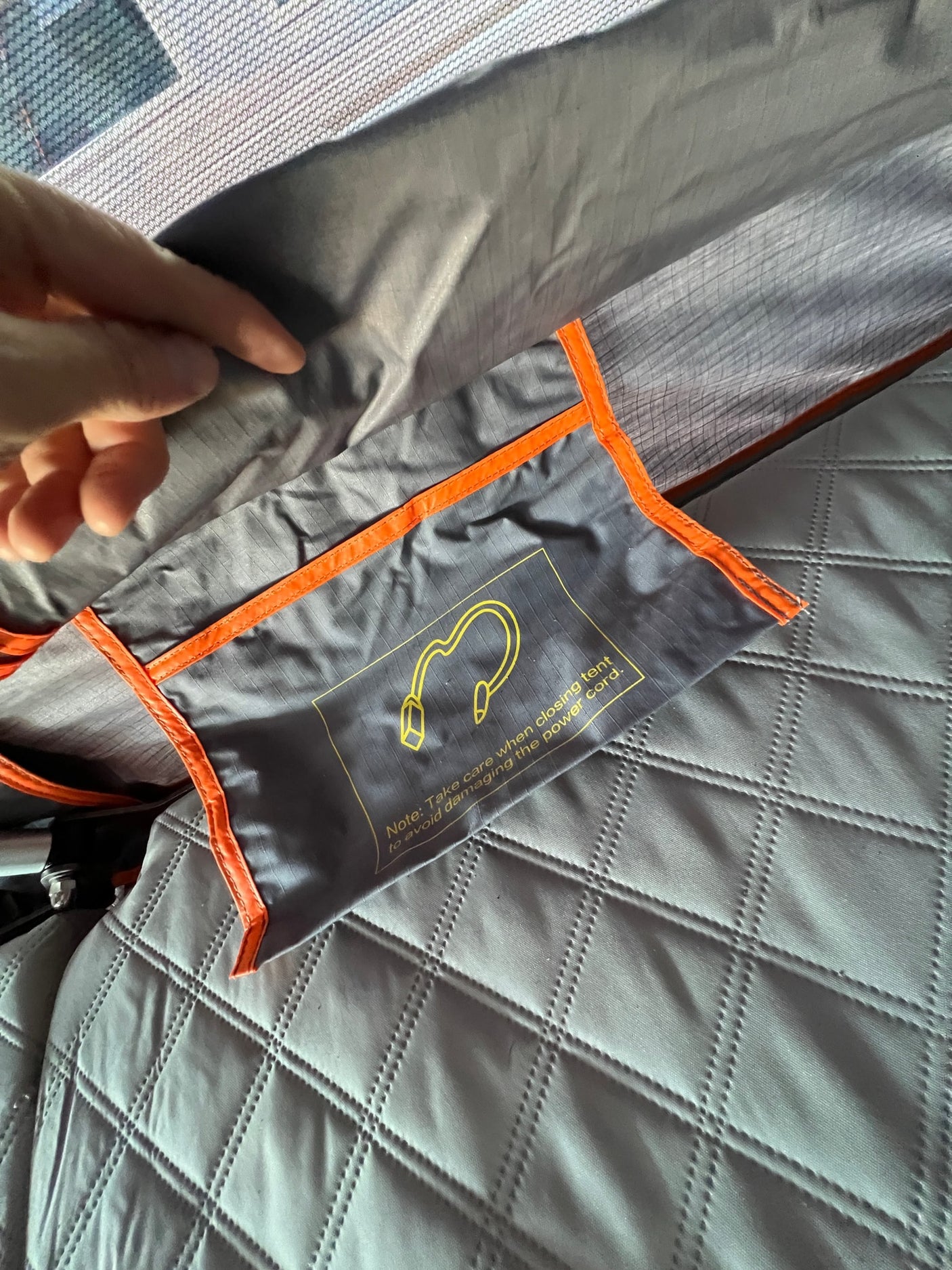 RV rental interior: a safety note on a pouch warns to protect the power cord when closing the tent, by quilted bedding.