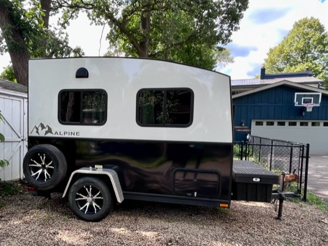 A sleek black and white Alpine compact travel trailer with a utility deck, ready for your next RV rental adventure.