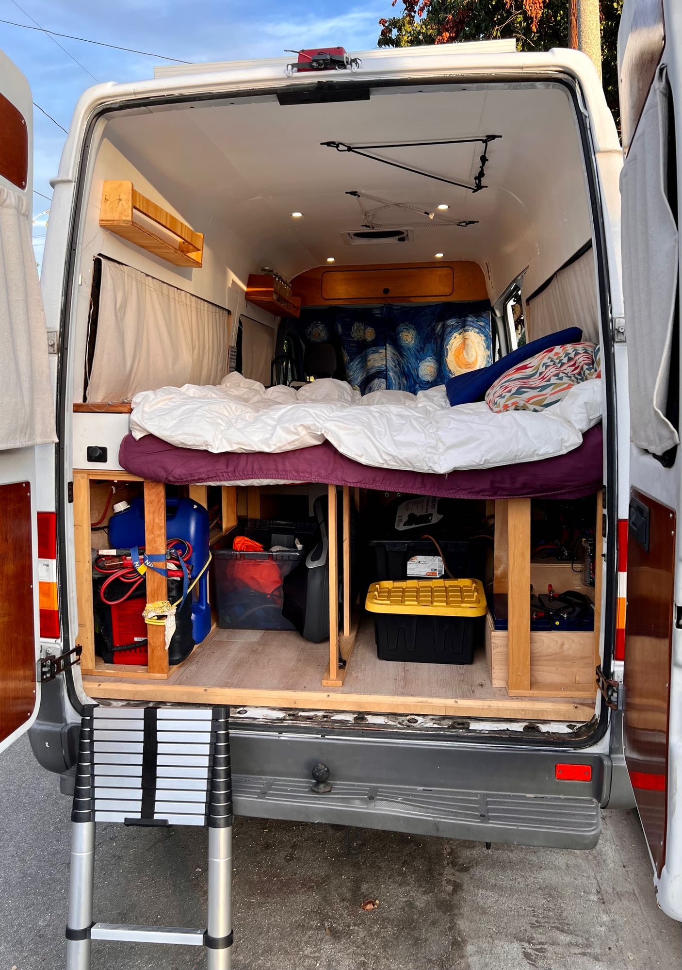 Inside an RV rental camper van: raised bed, ample under-bed storage, Starry Night decor, and ladder access.
