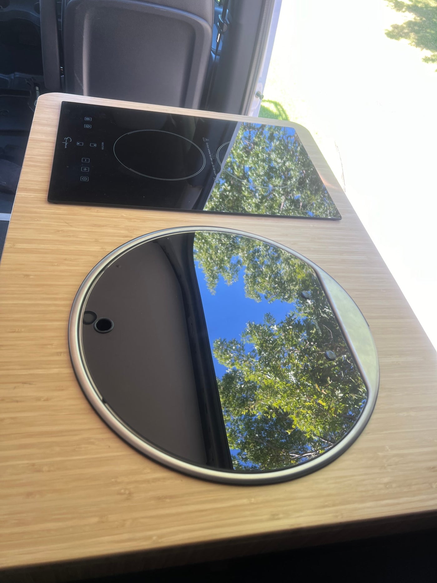 Compact RV rental kitchen: bamboo counter, induction cooktop, and covered sink reflecting sunny sky & trees. — photo 9