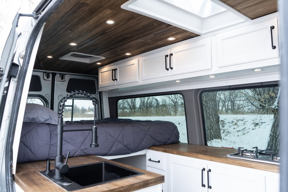 Spacious modern RV rental interior with cozy bed, kitchen sink, stove, wood accents, and scenic window views.