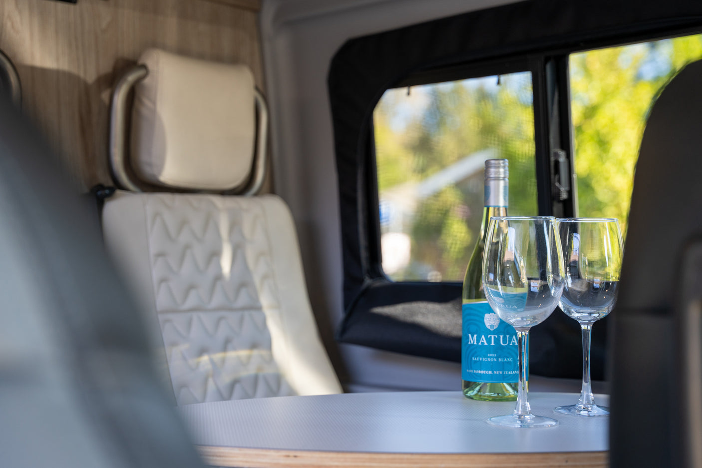A bottle of Matua Sauvignon Blanc wine and two glasses are on a table inside a comfortable RV rental, ready for relaxation.