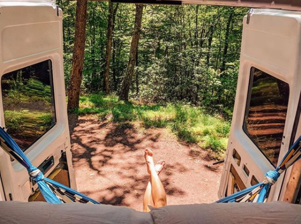 RV rental adventure: Legs crossed, relaxing inside a camper van, overlooking a sun-dappled forest path.