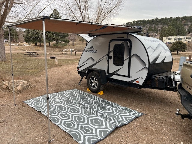 parked among vibrant yellow fall aspen trees.|White "FREESOLO" teardrop RV rental parked at a mountain campsite