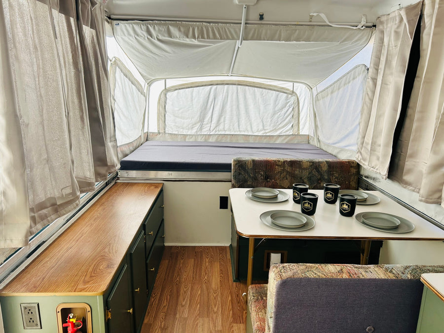Inside a bright pop-up rv rental, featuring a bed, dining table with dishes, and cabinet storage.