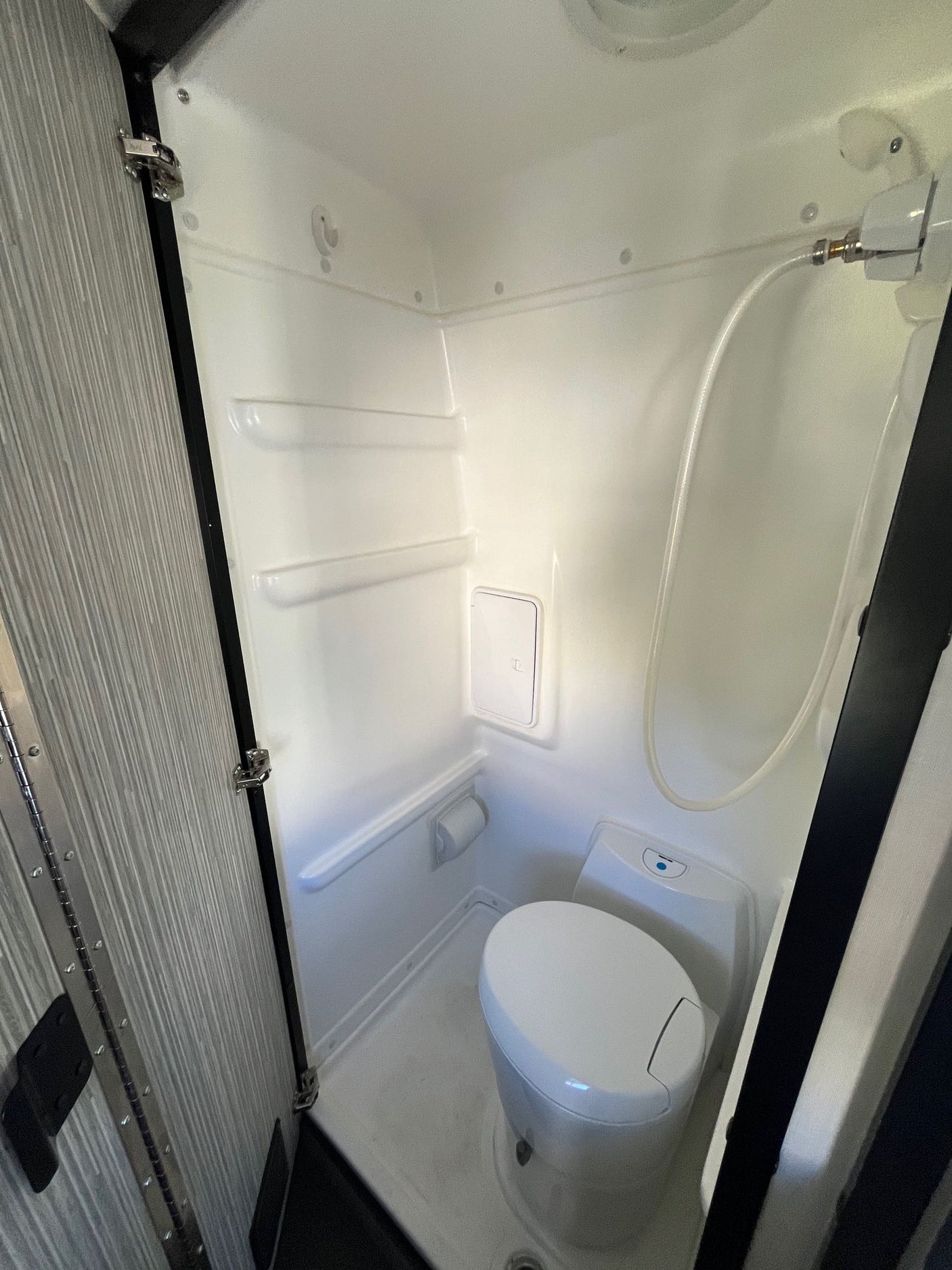 Explore this clean, compact RV rental wet bath, featuring a white toilet, shower hose, and built-in shelves.