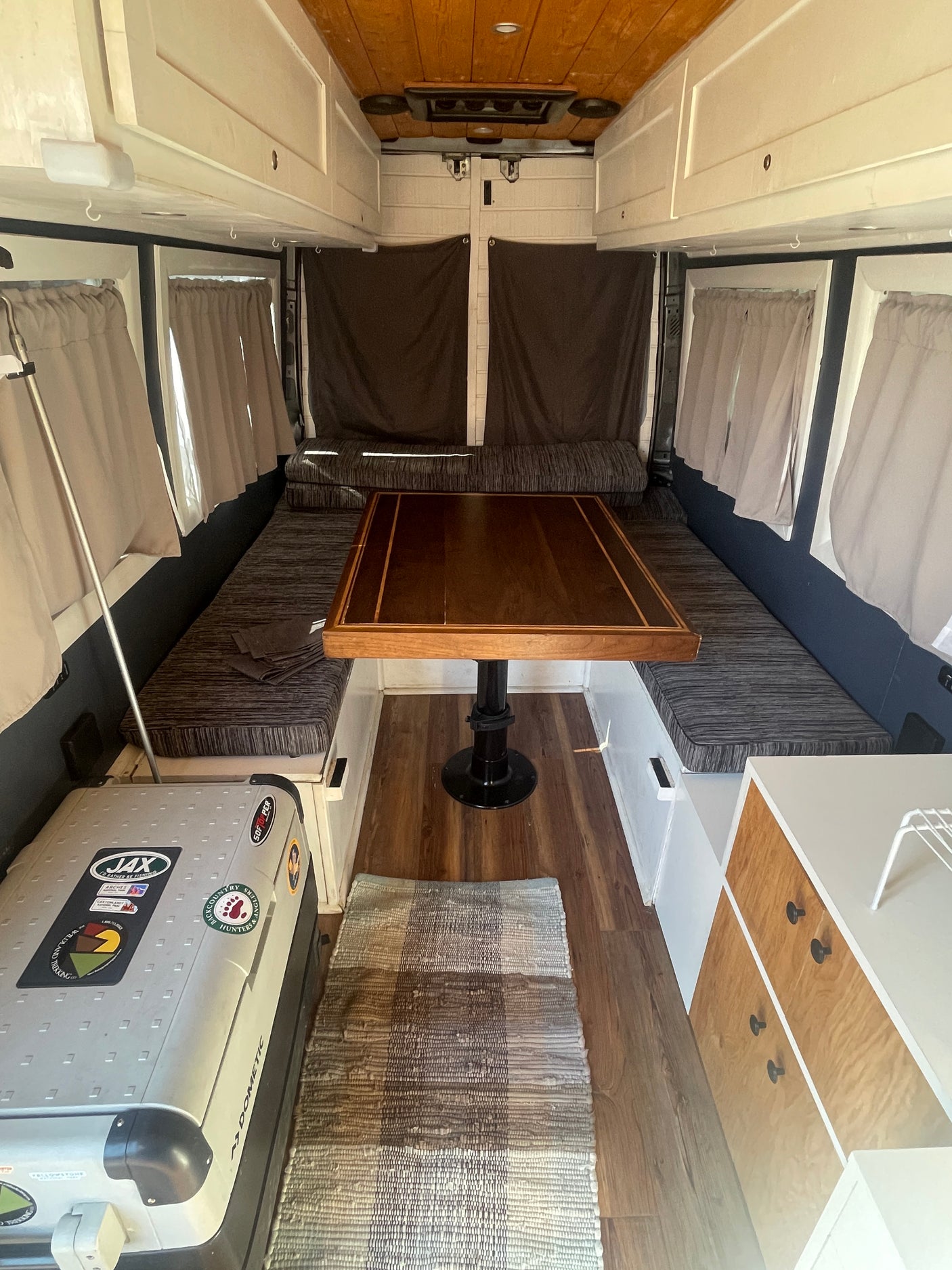 This RV rental interior features a dinette, overhead cabinets, and a Dometic cooler, ideal for camper van adventures.