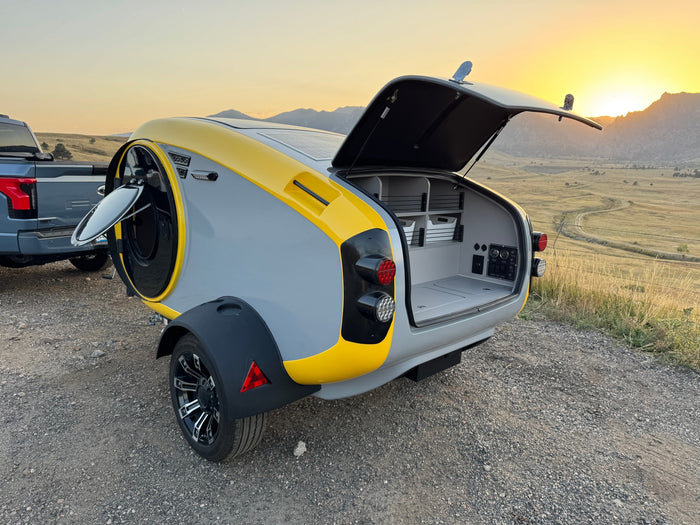 Modern, solar-powered teardrop camper hitched to a truck, ready for your next RV rental adventure in the mountains.