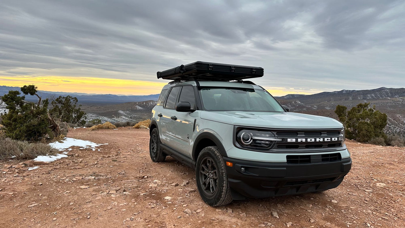 a unique RV rental alternative for scenic overlanding in the mountains.|A Ford Bronco Sport with rooftop tent on rugged terrain. Perfect for scenic outdoor adventure. Consider an RV rental for your next trip.|A grey Bronco Sport with a rooftop tent & awning