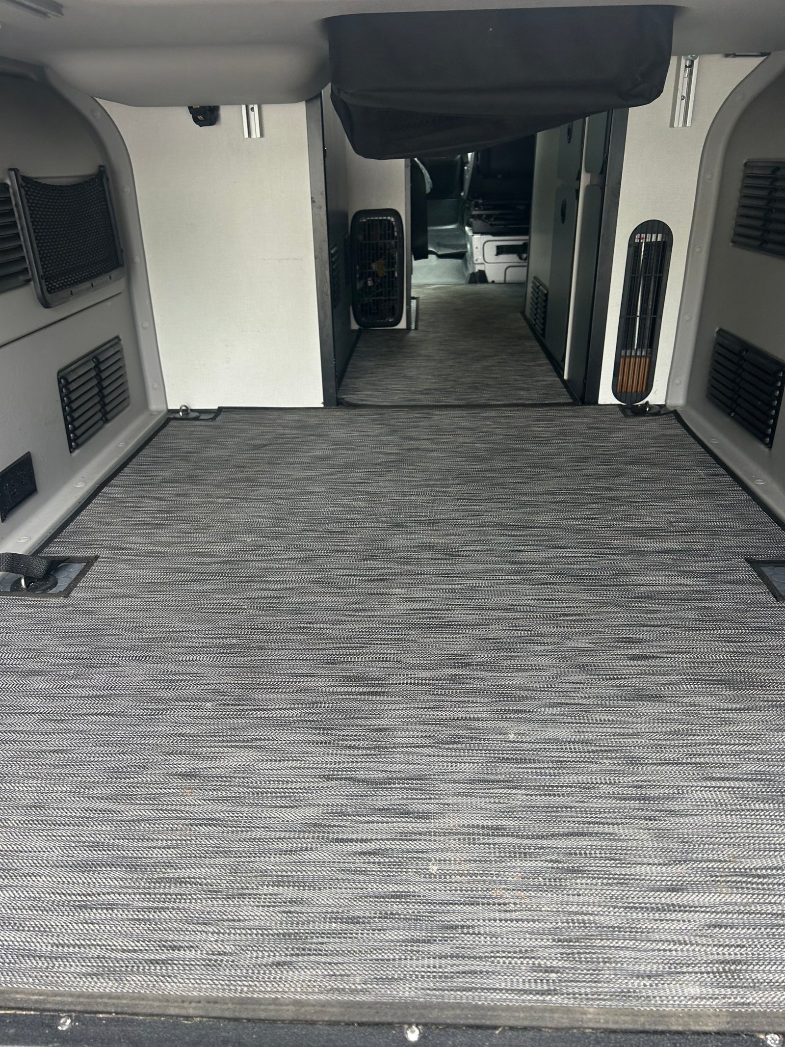 RV rental interior: Spacious cargo/living area with gray textured flooring, side panels, vents, and tie-downs, leading to the cab.