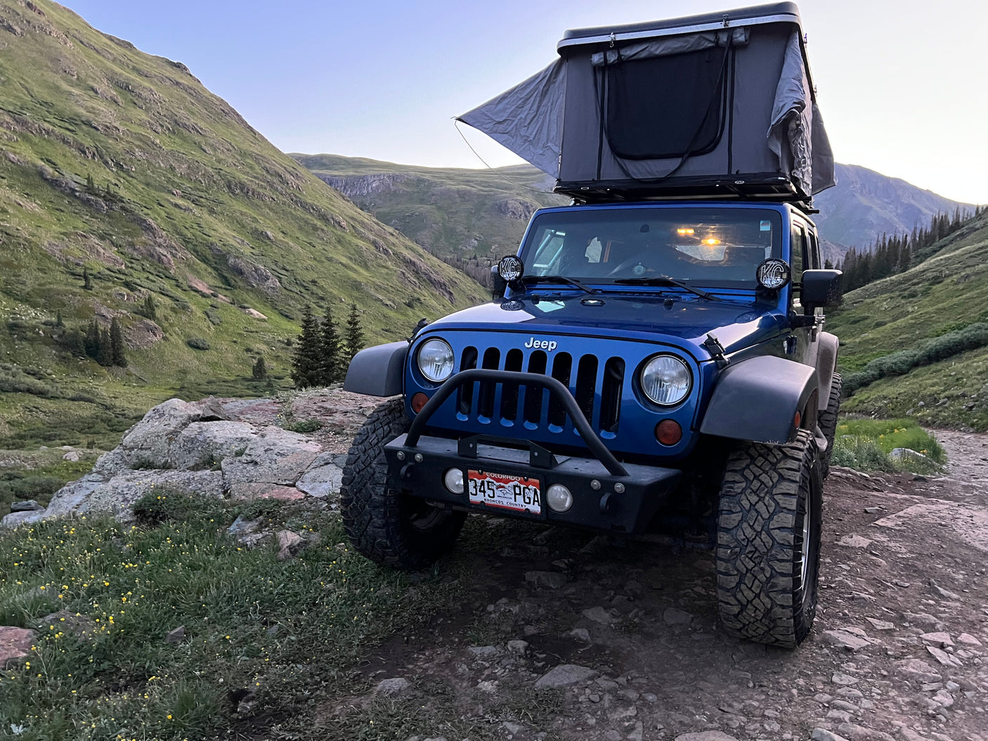 Blue Jeep with rooftop tent on mountain trail. Perfect for off-grid adventure, like an RV rental for rugged exploration.