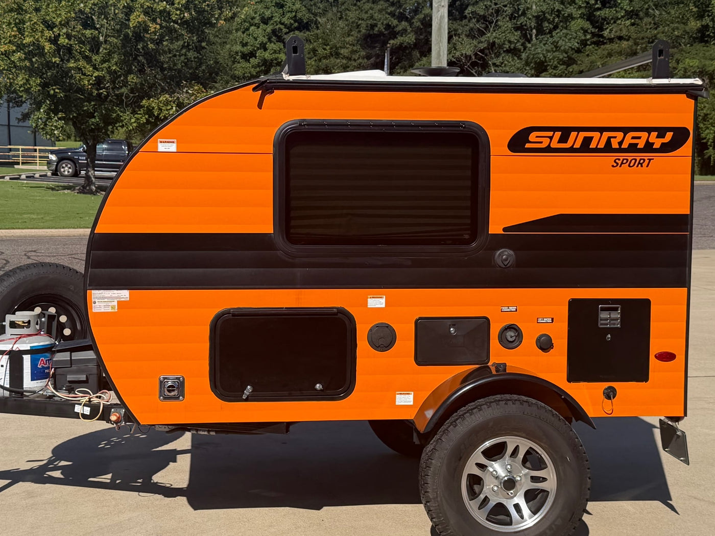 featuring rugged tires.|Orange and black SunRay Sport teardrop RV rental parked outdoors — photo 3
