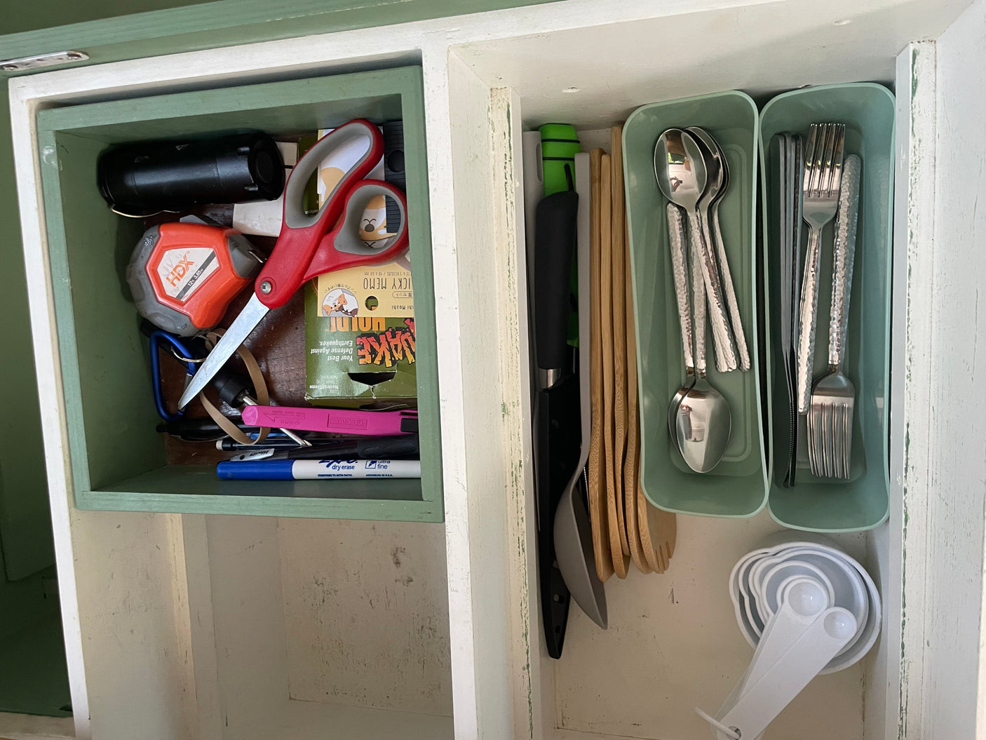 This RV rental cabinet features organized tools like a tape measure and scissors, alongside kitchen utensils and measuring cups.