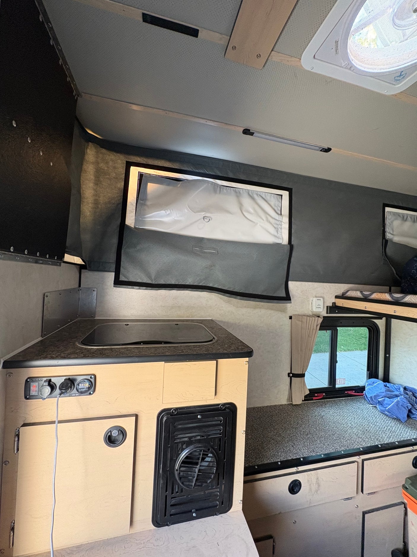 Compact RV rental interior featuring a kitchenette, bed area, and pop-up camper design with fabric walls and a roof vent.