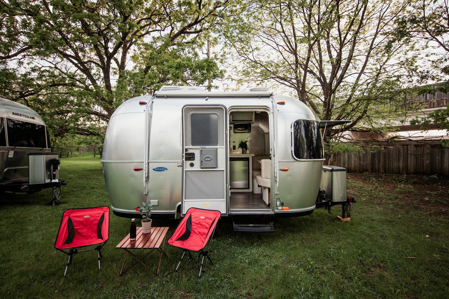 Silver Airstream rv rental with open door showing its interior, plus red chairs & a table outside in a grassy, treed setting.