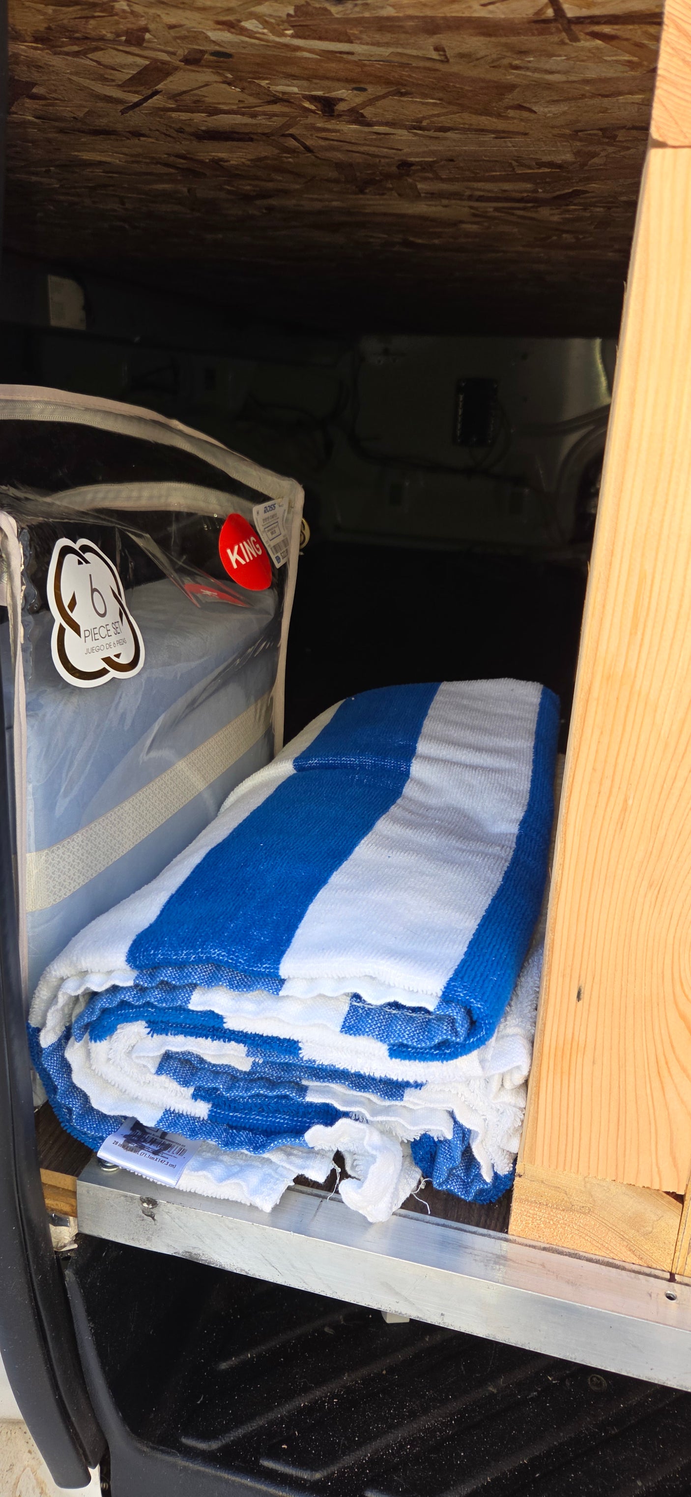 Bedding and blue/white towels neatly stowed in an RV rental's storage space.