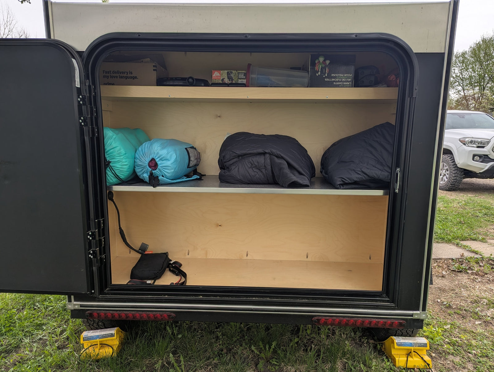 This RV rental's organized storage compartment holds sleeping bags, a portable shower, and other camping essentials on shelves.