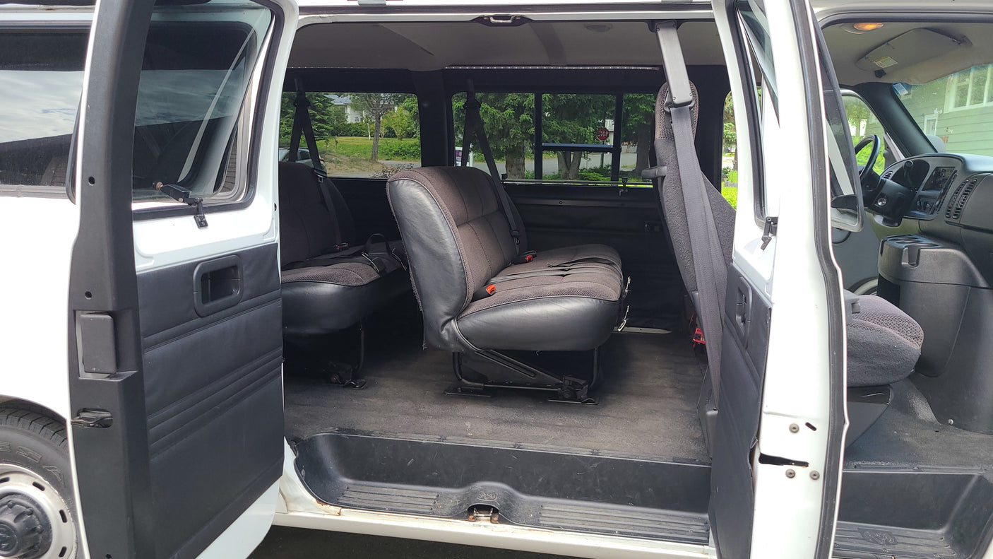 Spacious white van interior with two rows of dark passenger seats and open side doors, perfect for an RV rental adventure.