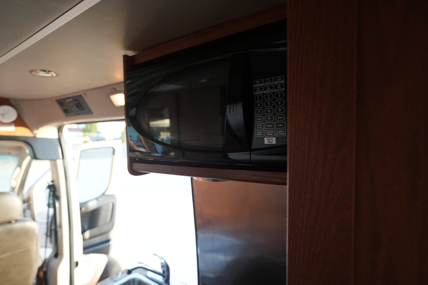 Black microwave oven mounted in an rv rental, with its control panel showing options like Popcorn, Pizza, and Defrost.