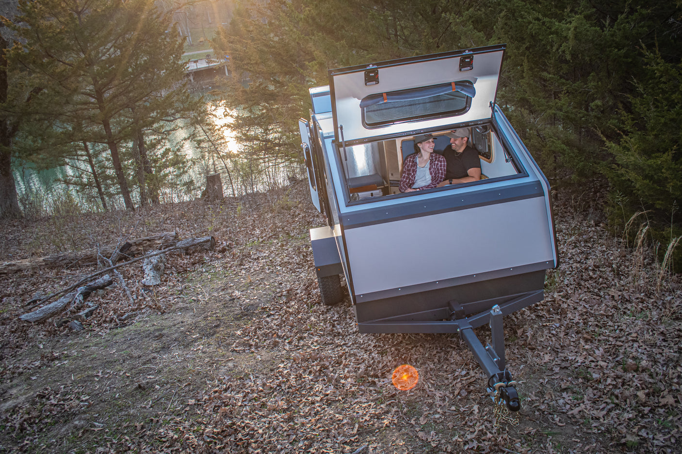 Couple enjoys a unique view from their modern RV rental with an open roof hatch, overlooking a tranquil lake.
