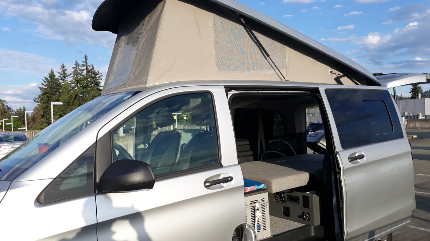 Compact silver camper van with pop-top roof open, showing interior, ready for rv rental adventures.
