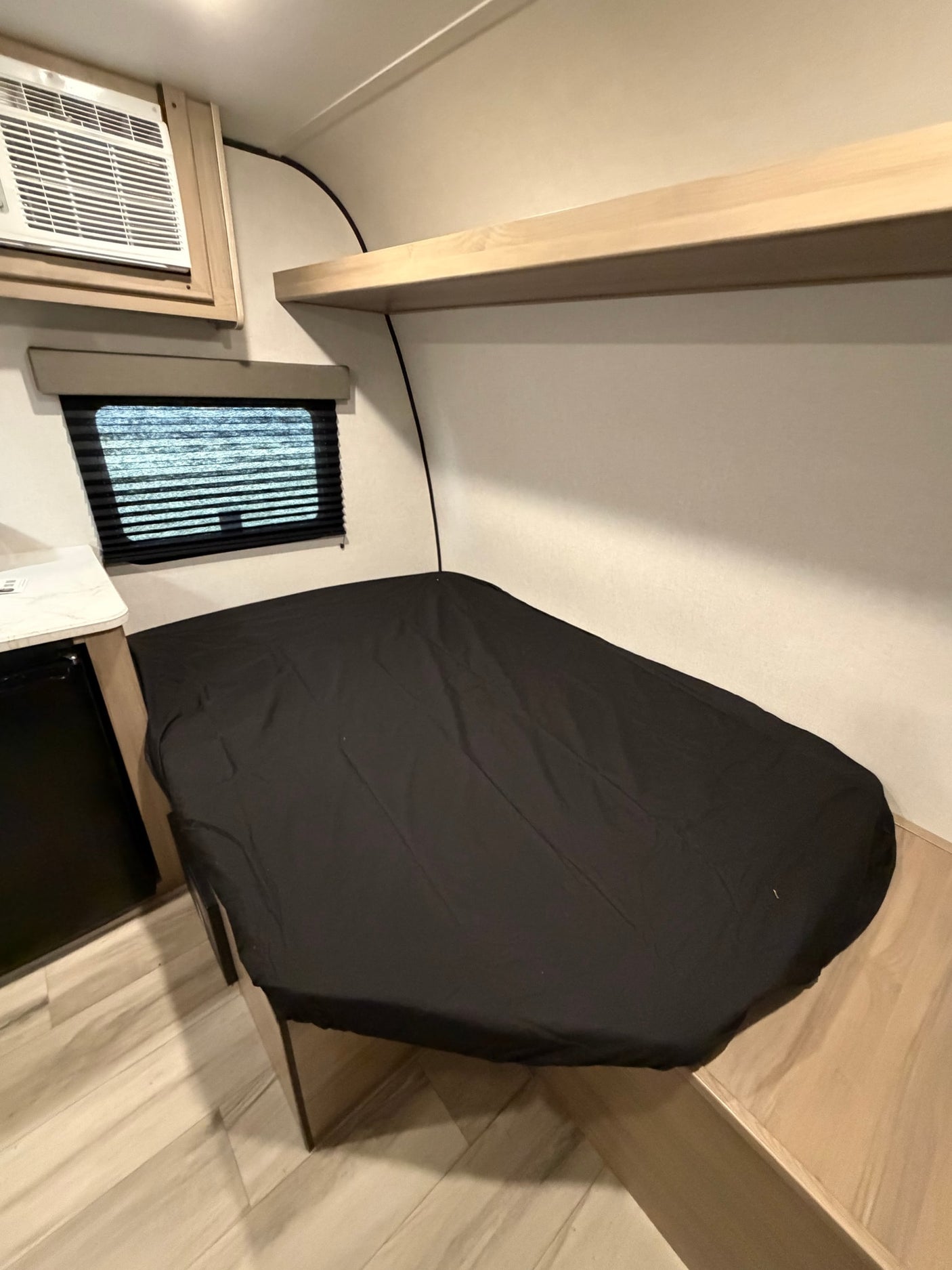 This cozy RV rental features a compact sleeping area with a comfortable bed, window with blinds, and air conditioning unit.