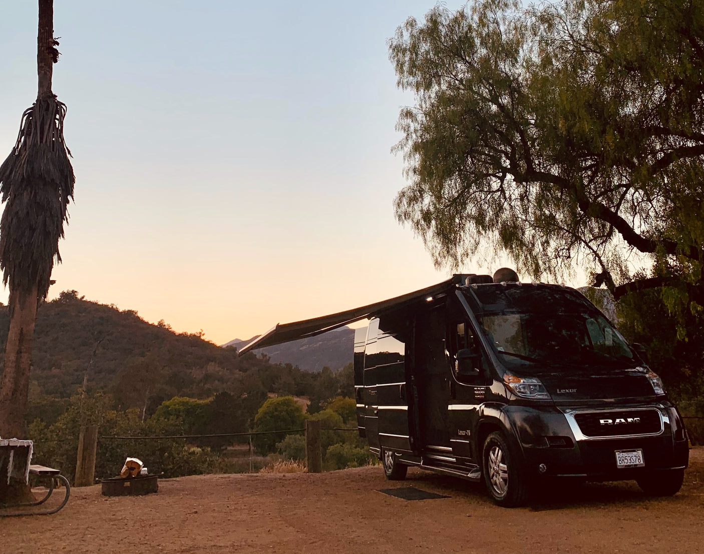 Enjoying a beautiful sunset at a scenic campsite with an extended awning from a black rv rental camper van, ready for adventure.