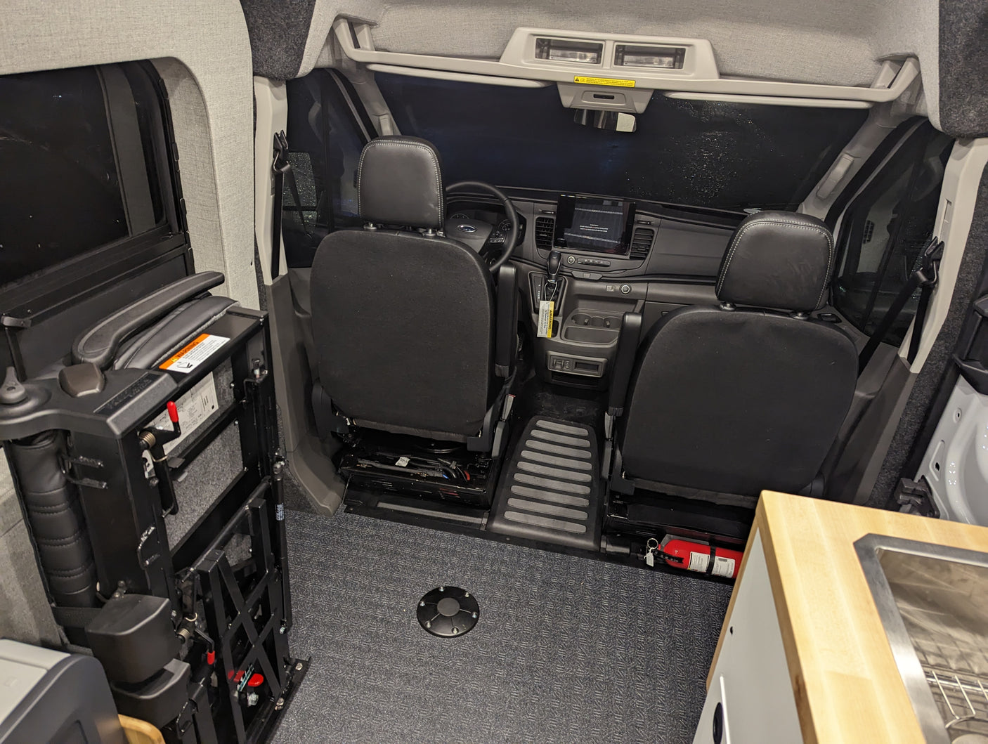 Interior of an RV rental van showing front seats, dashboard, and a deployed wheelchair lift for accessible travel.