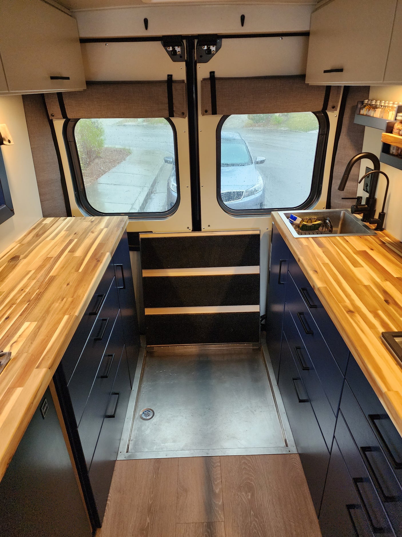 Custom RV rental interior with a modern kitchen, wooden counter, sink, and integrated shower. Ideal for trips.
