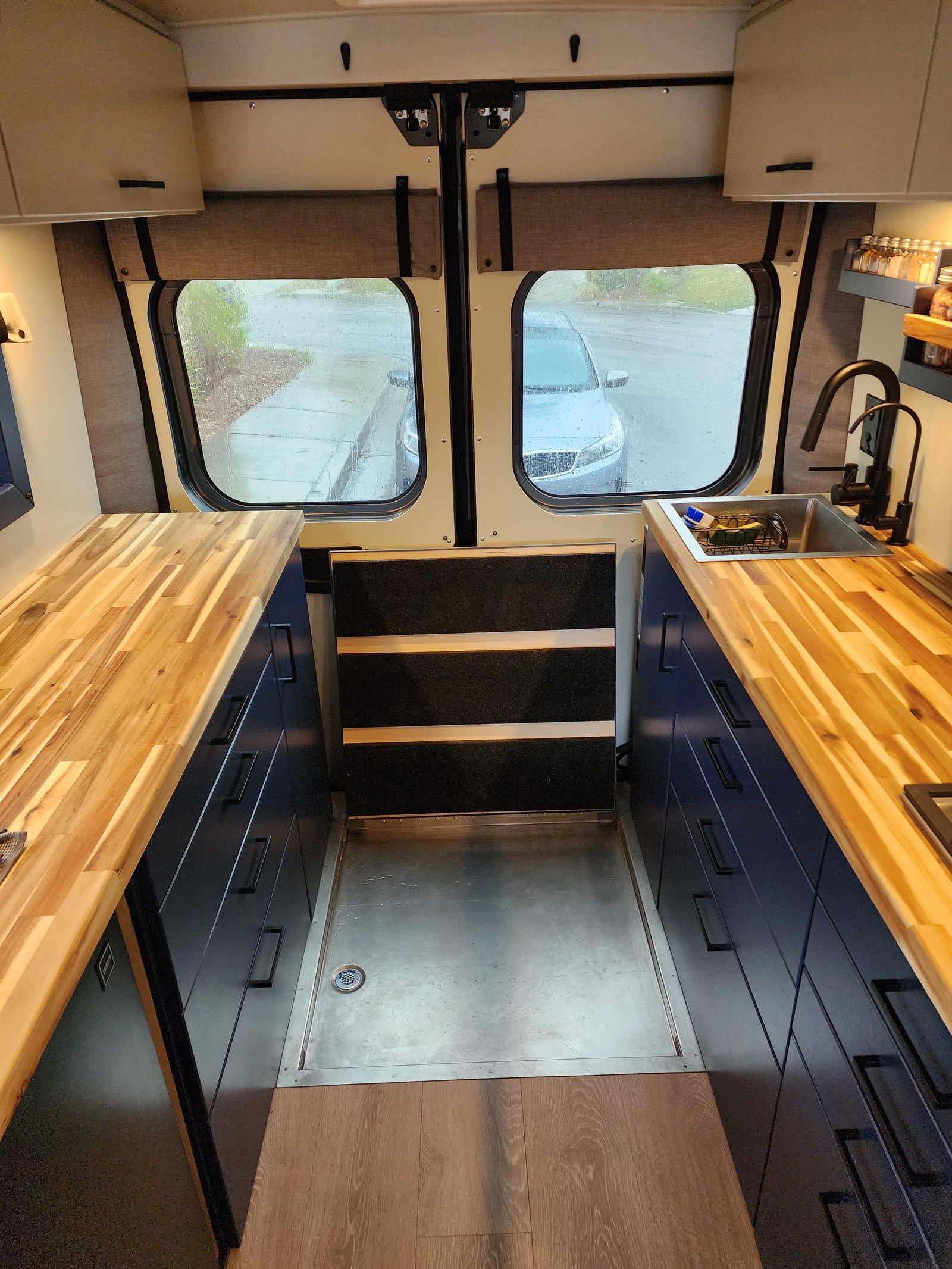 Custom RV rental interior with a modern kitchen, wooden counter, sink, and integrated shower. Ideal for trips.