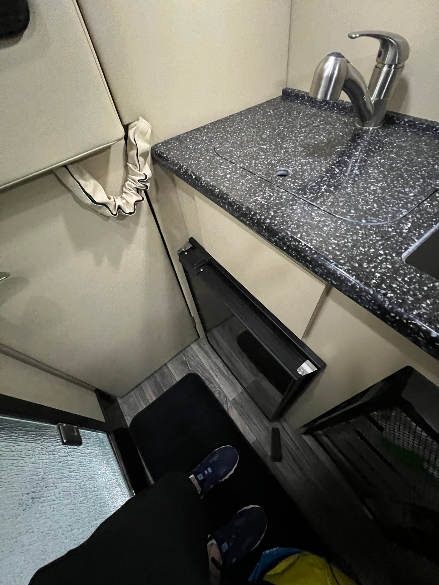 View of an rv rental interior: compact kitchen with dark speckled counter, sink, fridge, and light upholstered seating.