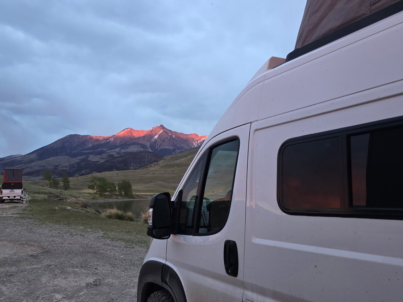 White camper van (rv rental) by a tranquil lake, mountains bathed in alpenglow. A perfect nature escape awaits.