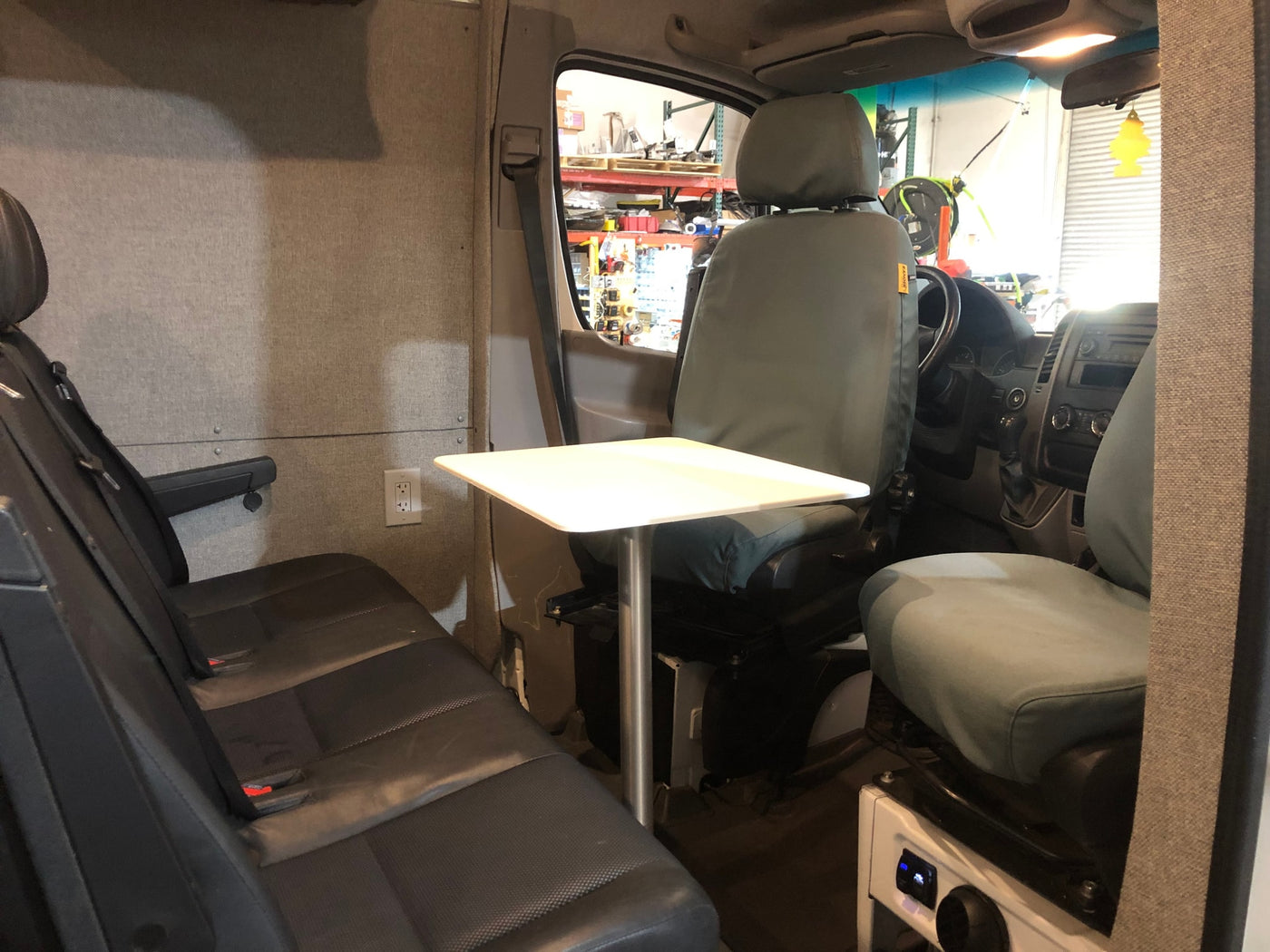 This RV rental interior features rear bench seating, a central table, and an electrical outlet, looking towards the front cabin. — photo 3