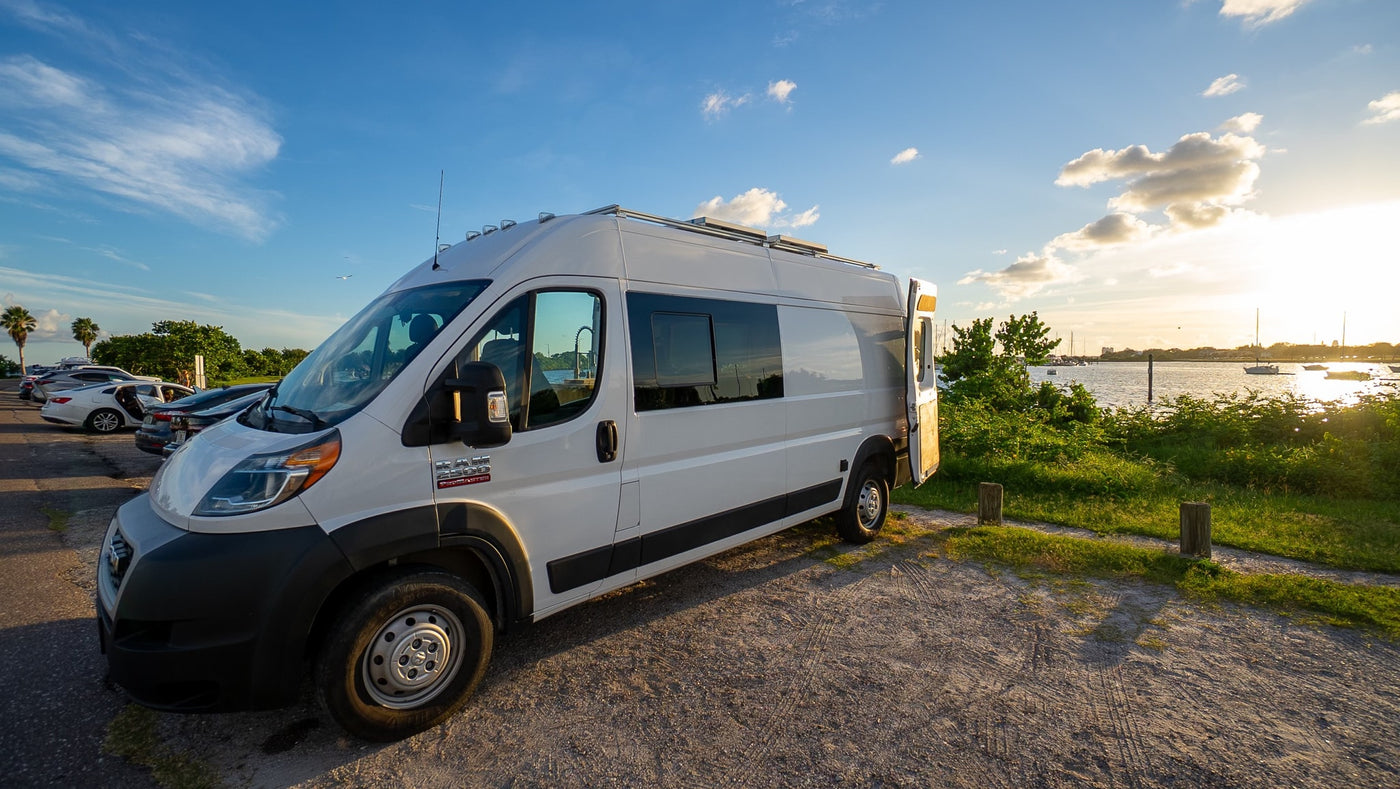 Enjoy scenic views with this rv rental! A white camper van is parked at a waterfront lot under a beautiful sunset sky. — photo 10