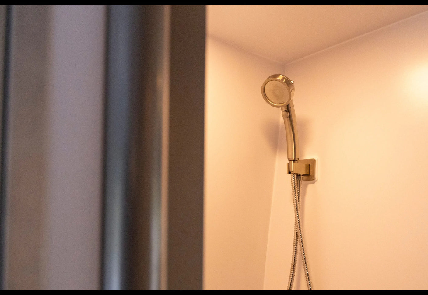 Close-up of a compact, metallic shower head mounted in a clean, warm-lit RV bathroom, ready for your rv rental.