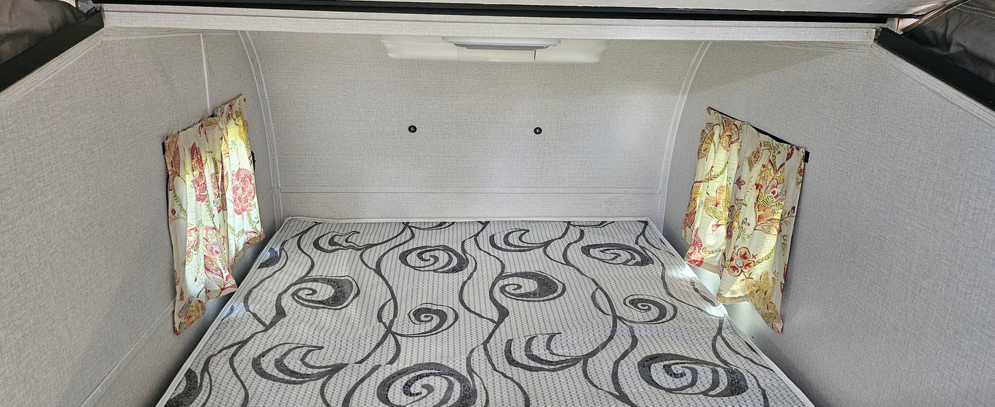 Cozy RV rental bedroom with a comfy patterned mattress, floral curtains, and light textured walls, perfect for camping adventures.