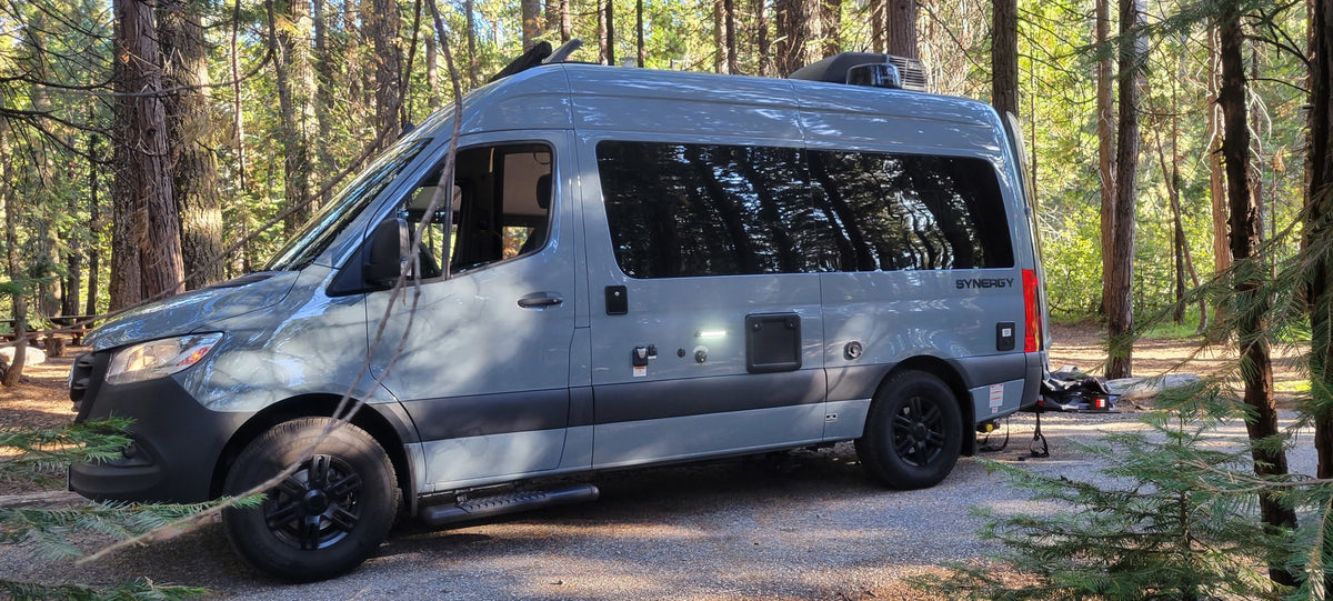Gray Mercedes Sprinter SYNERGY rv rental camper van parked at a sunny forest campsite with tall trees. — photo 2