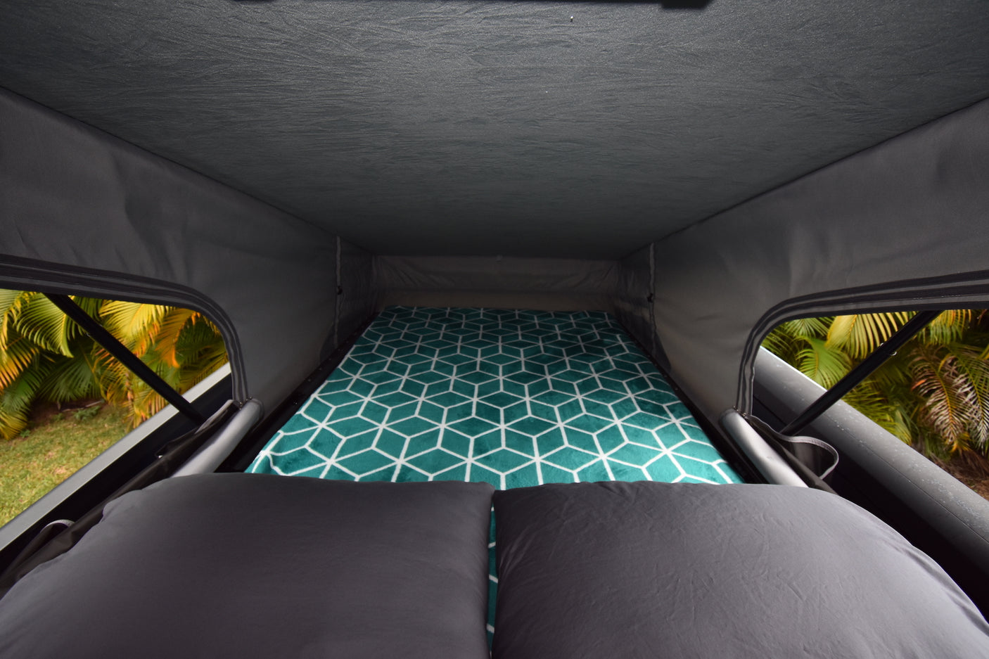 Enjoy this RV rental pop-top camper interior: a comfy bed with a geometric pattern & stunning nature views.