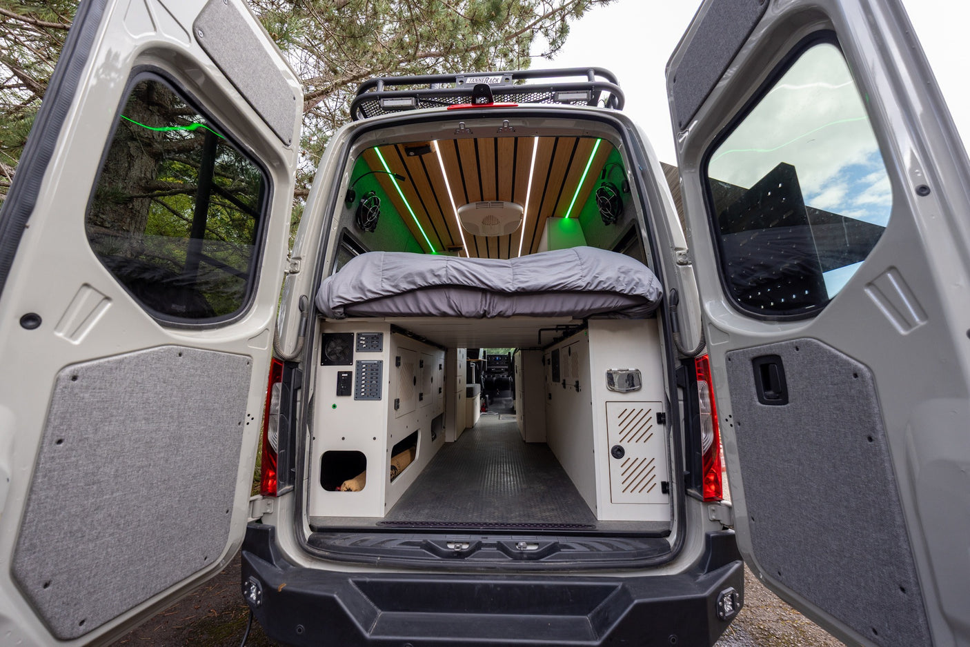 Inside an RV rental campervan: modern interior with a cozy bed, custom storage, and vibrant green LED lighting.