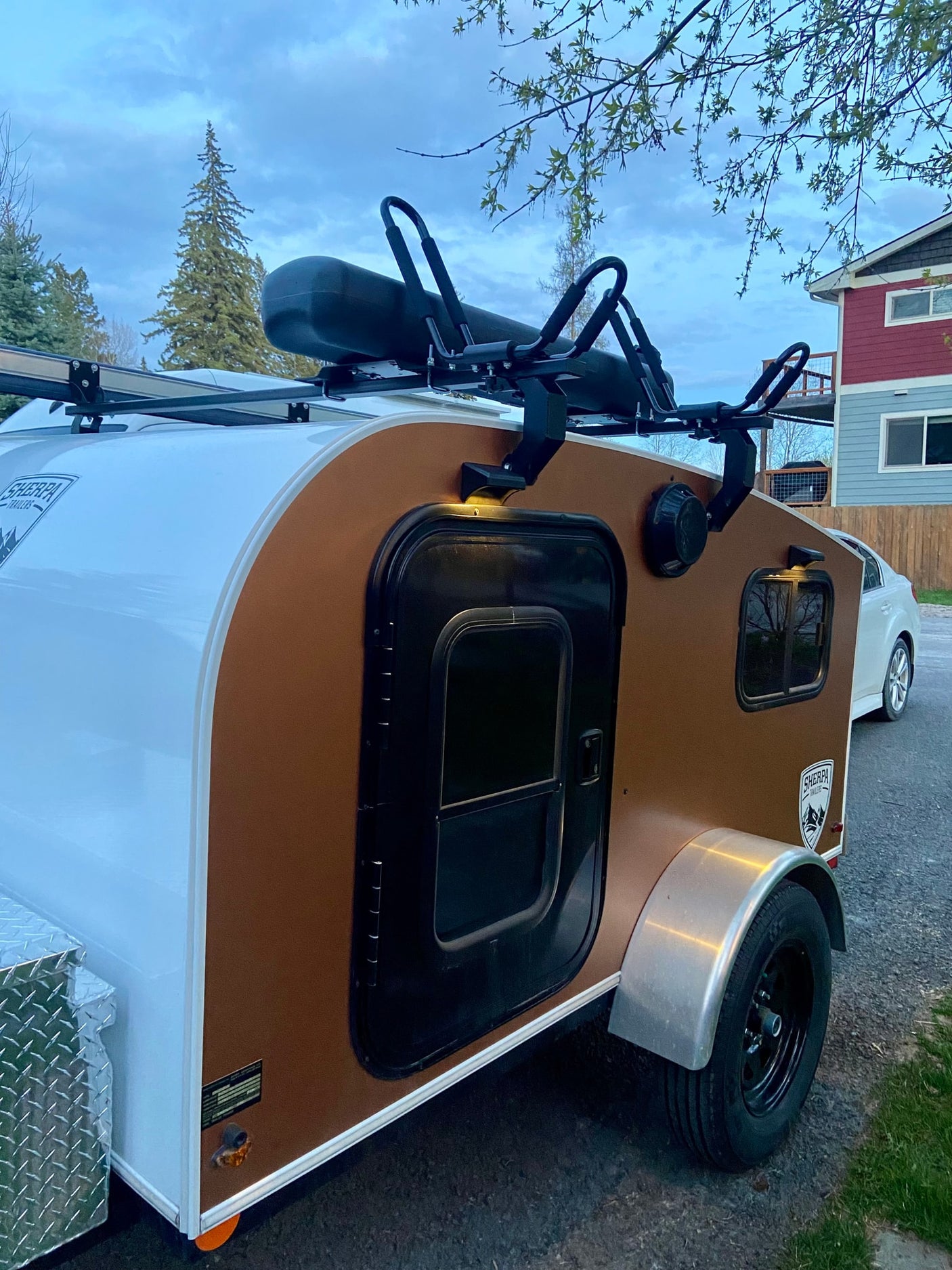 A compact brown and white Sherpa teardrop camper with rooftop rack, ideal for your next RV rental outdoor adventure.
