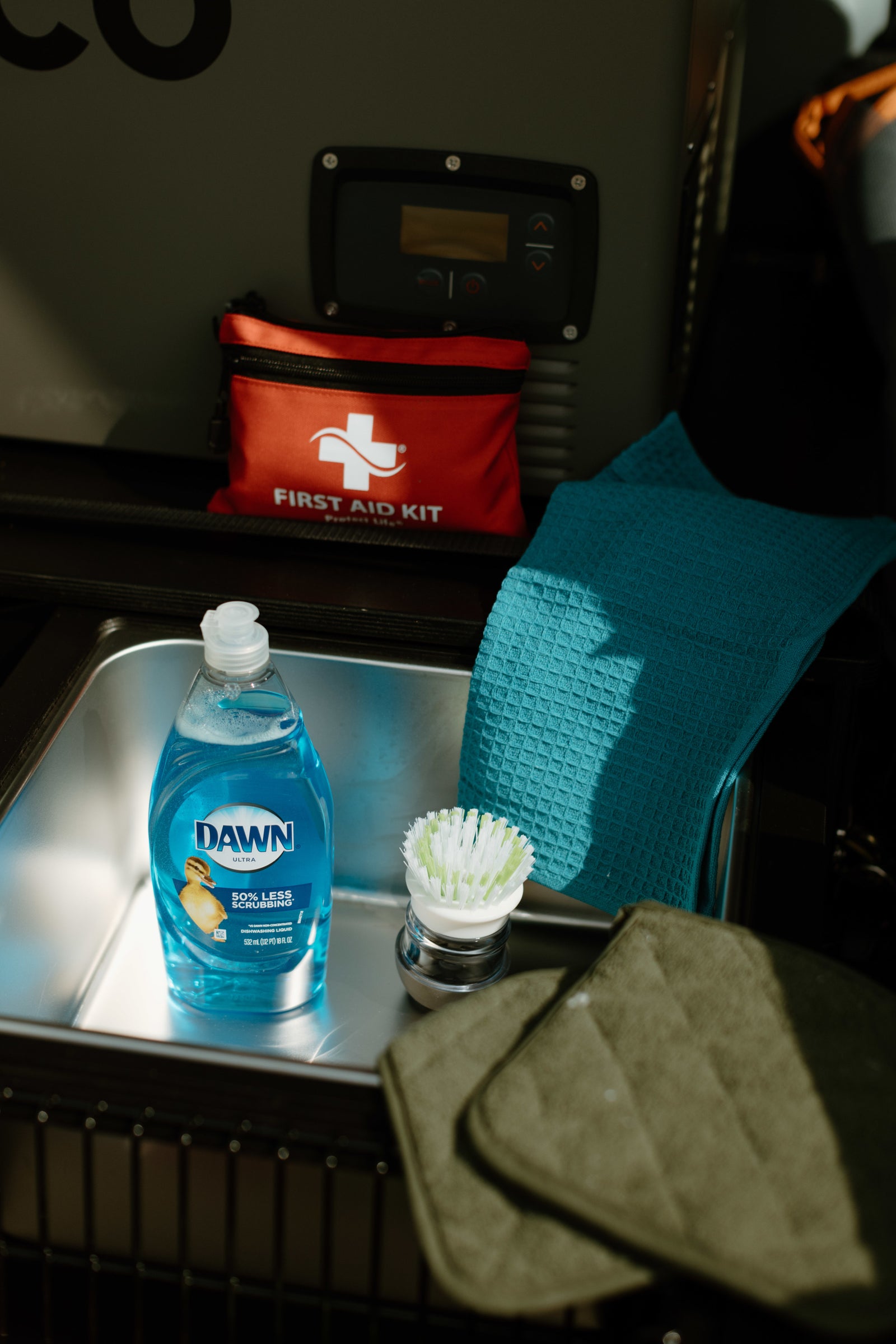RV rental ready: Dawn dish soap, brush, towels, and a first aid kit set up in a compact sink area.