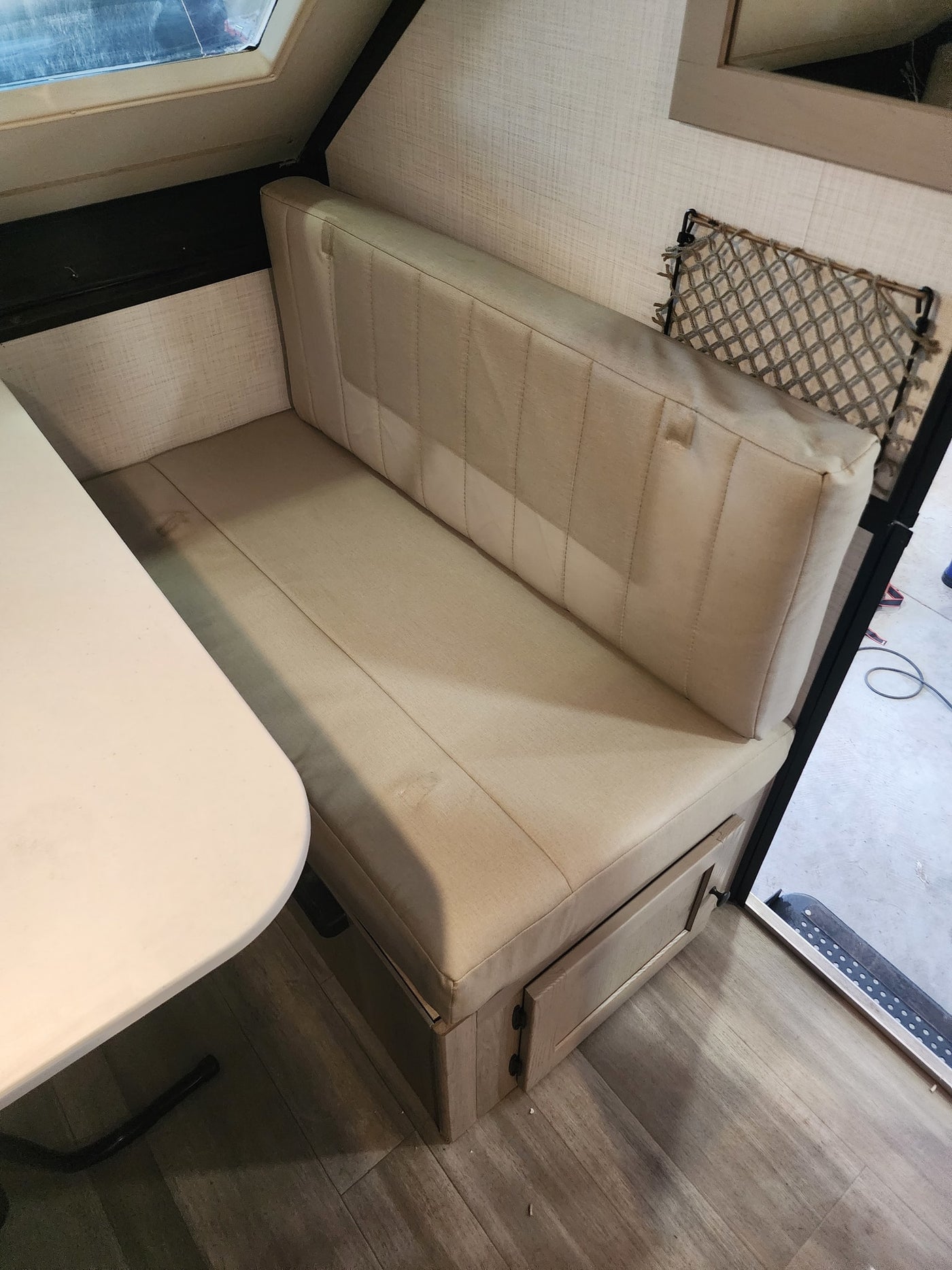 RV rental interior featuring a dinette bench with light cushions, a table, wood-look flooring, and a storage net. — photo 7