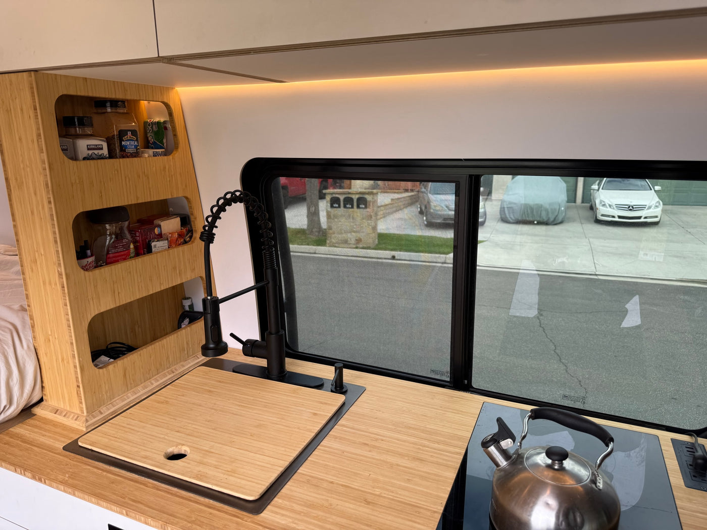 This RV rental's modern bamboo kitchen offers a sink, stovetop, and organized storage, with a view outside. — photo 10