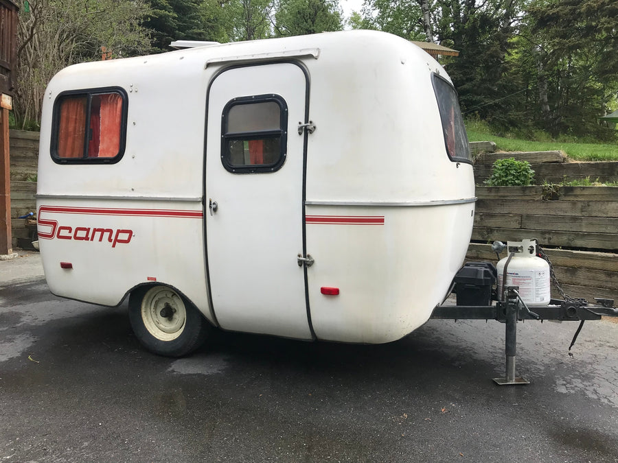 A compact white Scamp travel trailer, complete with a propane tank, ready for an RV rental adventure.