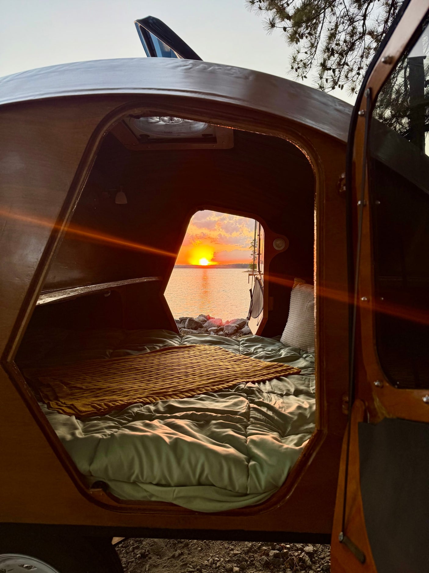 and a yellow throw. Perfect for outdoor camping adventures.|This unique wooden teardrop camper by a lake