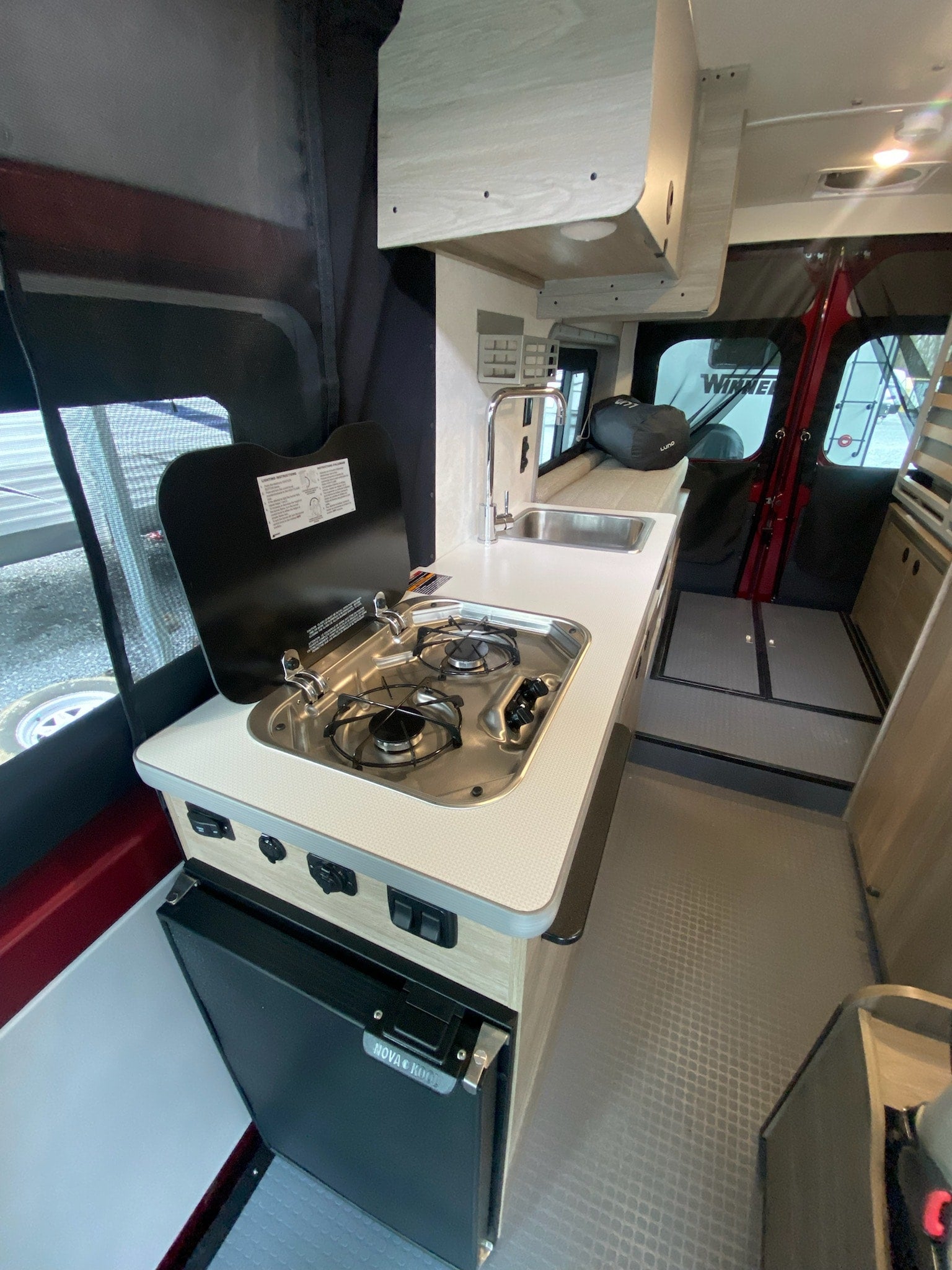 Explore the compact and functional interior of an RV rental camper van, featuring a kitchenette with a sink, stove, and fridge.