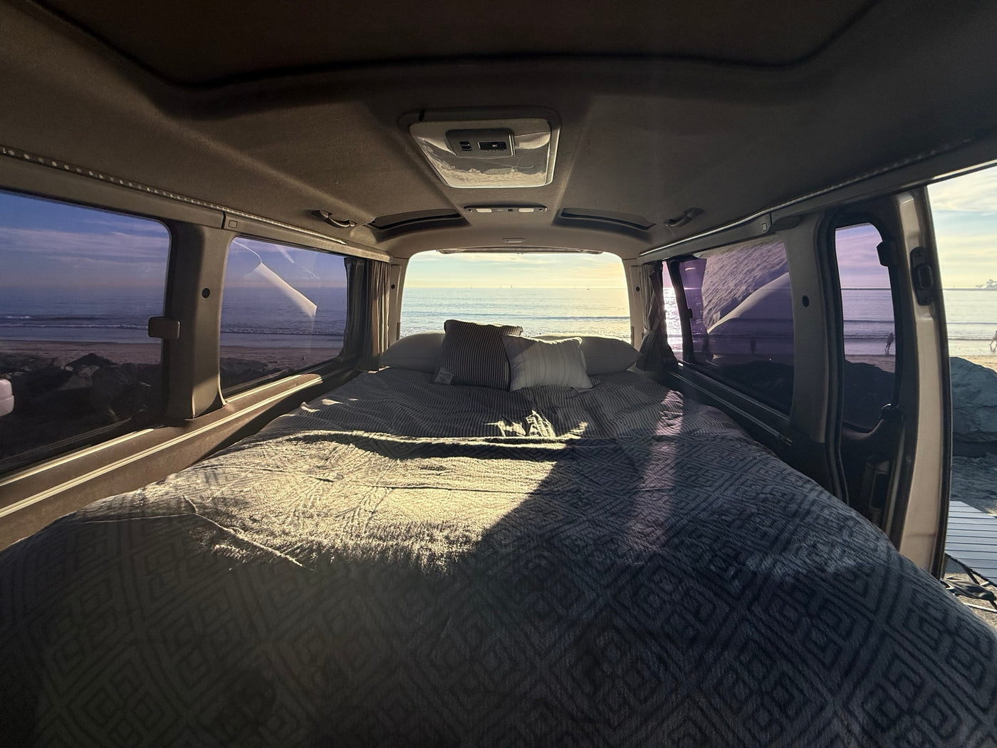 and cornhole outside by the ocean.|This RV rental offers a cozy campervan interior with a bed — photo 4
