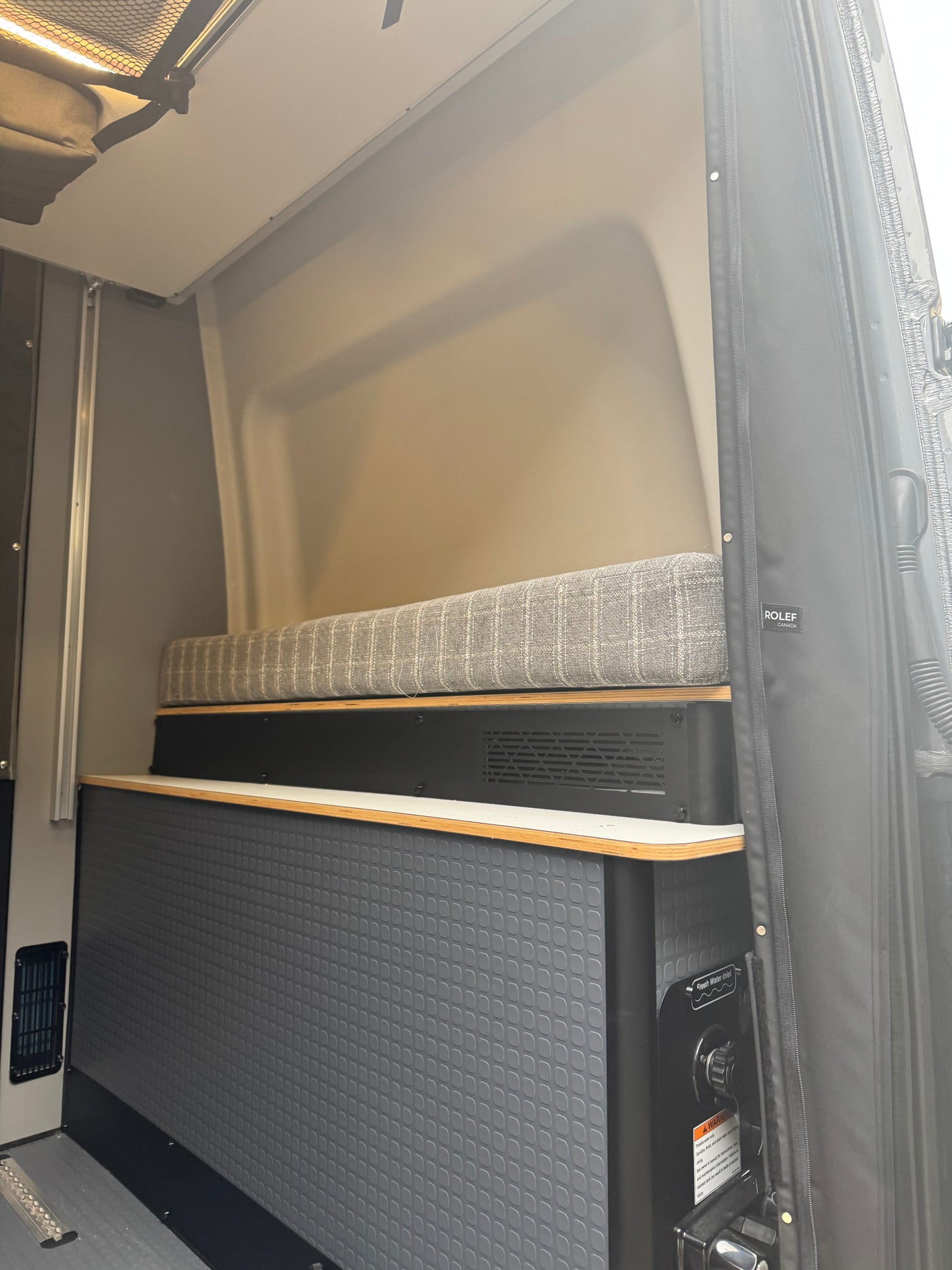 RV rental interior featuring a cushioned bench, lower textured cabinetry, and a fresh water inlet.