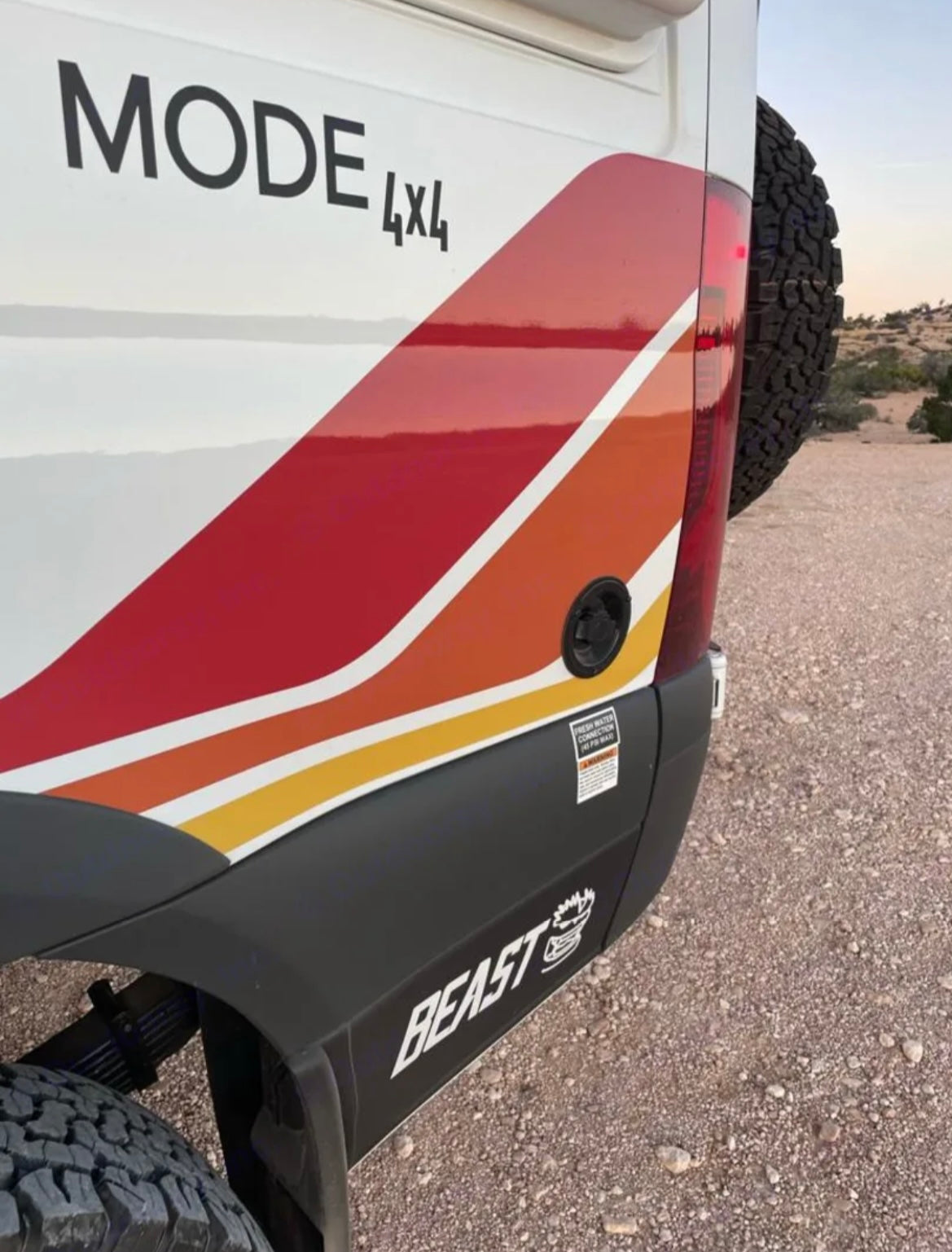 Rear view of a white MODE 4x4 rv rental camper van with retro red/orange/yellow stripes and 'BEAST' branding for off-road travel.